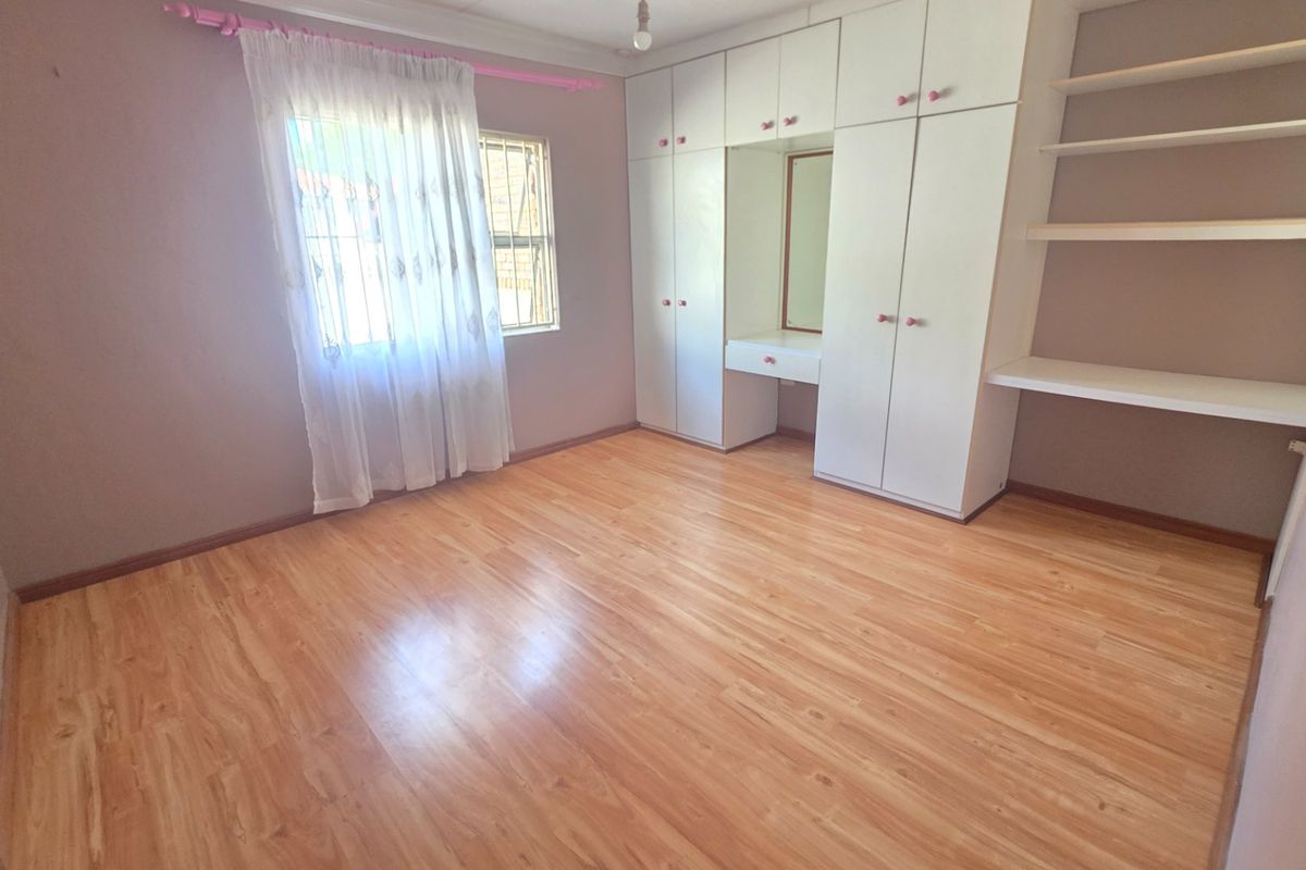 A spacious bedroom featuring light wood-look laminate flooring, extensive built-in cabinetry with a vanity area, and built-in shelving.