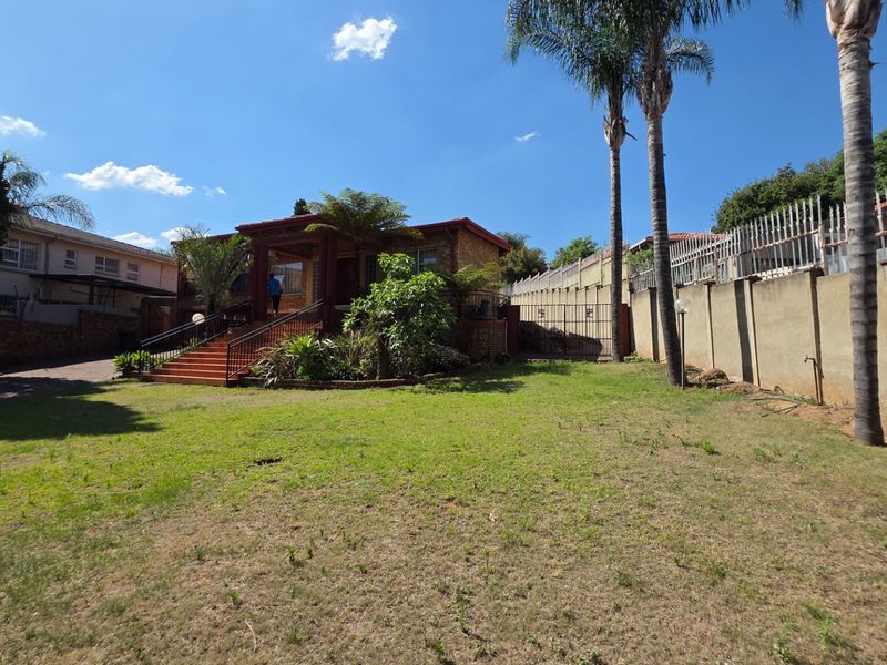 Front view of a brick house featuring a covered entrance porch, concrete stairs with metal railings, and a spacious front garden with perimeter walling.