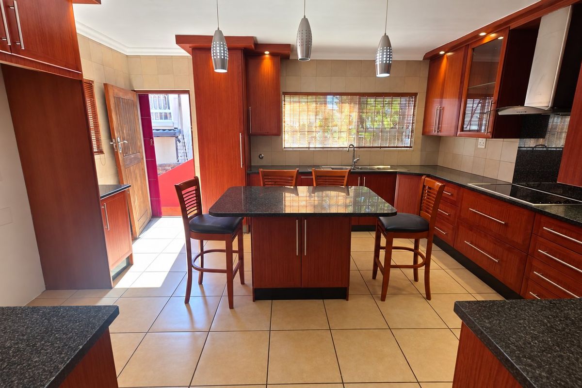 A well-maintained kitchen featuring warm-toned wooden cabinetry, granite countertops, a central island, and tiled flooring with direct access to an outdoor area.