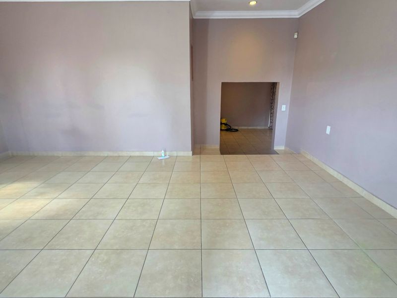 A spacious, empty living area featuring neutral tiled flooring, coved ceilings, and recessed lighting, offering a blank canvas for interior design.