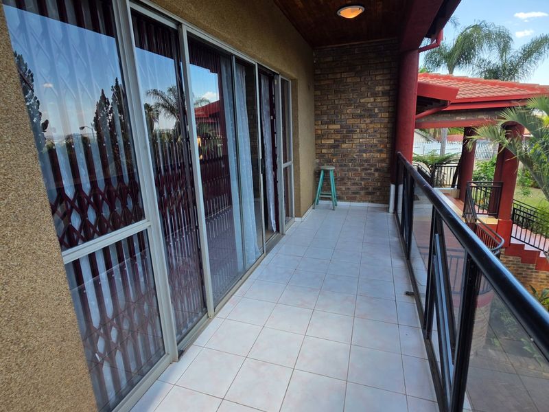 A covered balcony featuring tiled flooring, a brick feature wall, and a glass balustrade overlooking the garden area.