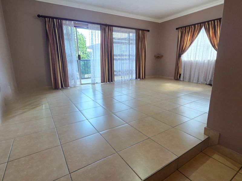 Spacious, empty living area featuring neutral ceramic floor tiles, large sliding glass doors with security gates, and ample natural light.