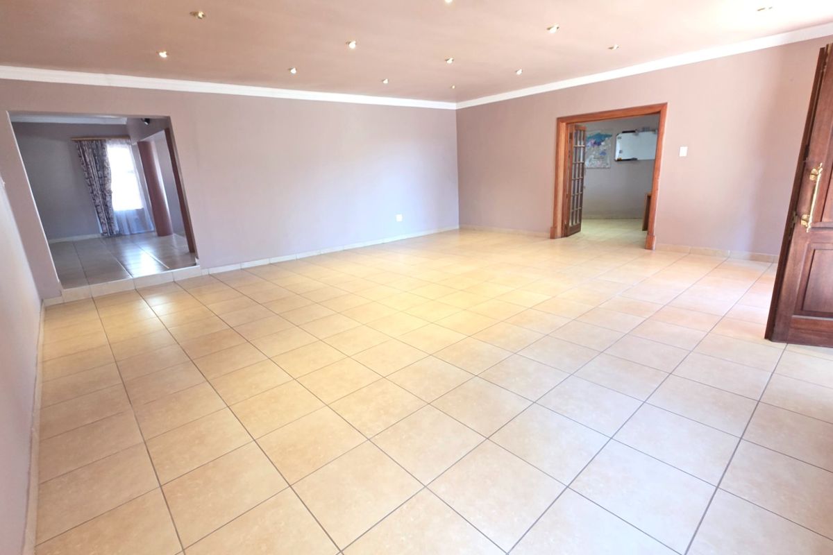 A spacious, empty living area featuring neutral wall tones, ceramic floor tiles, and recessed downlighting, providing a versatile blank canvas for interior design.