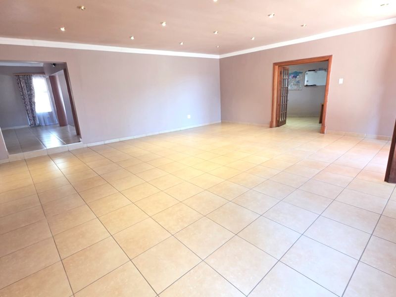 A spacious, empty living area featuring neutral wall tones, ceramic floor tiles, and recessed downlighting, providing a versatile blank canvas for interior design.