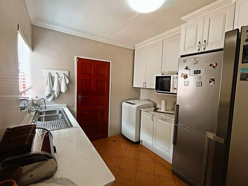 A functional kitchen featuring white cabinetry, a double bowl sink, built-in microwave space, and tiled flooring with direct access to an exterior door.