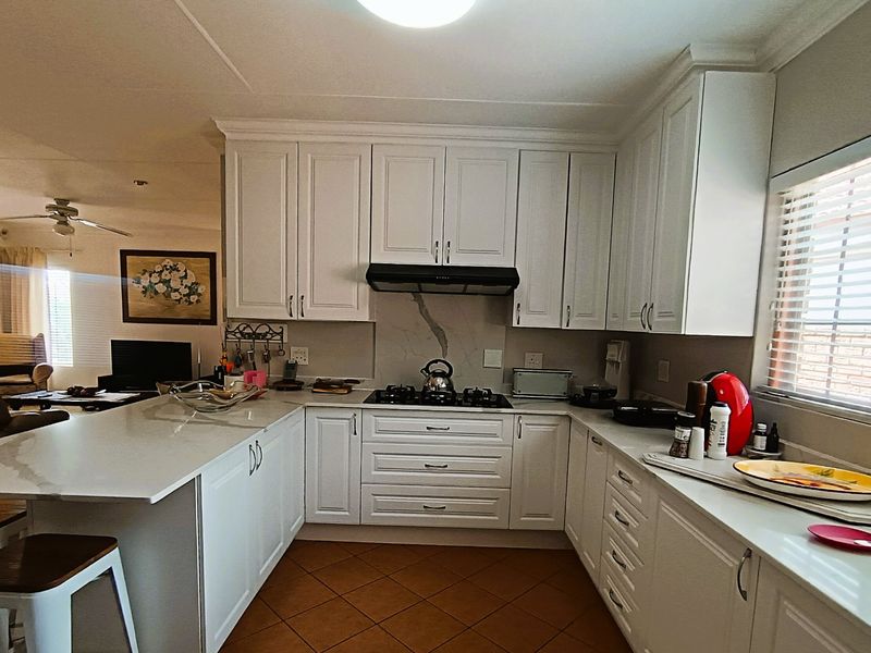 A well-maintained kitchen featuring white shaker-style cabinetry, stone countertops, a gas hob with extractor fan, and a functional breakfast bar layout.
