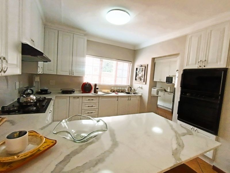 A well-appointed kitchen featuring white cabinetry, stone countertops, a central island, and integrated appliances, with an adjacent scullery area visible.
