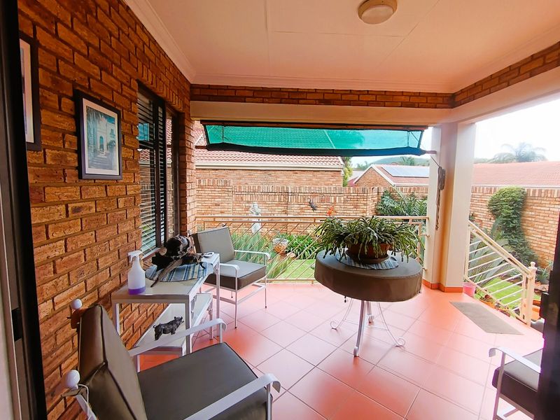 A covered patio featuring exposed brick walls, tiled flooring, and a metal balustrade, overlooking a garden area.