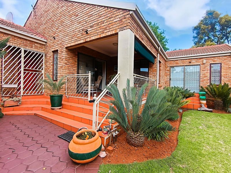 A well-maintained rear exterior view of a brick townhouse featuring a covered patio, paved outdoor area, and established garden.