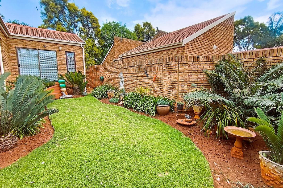 A well-maintained rear garden featuring a lush lawn, established landscaping, and face brick exterior walls with a tiled roof.