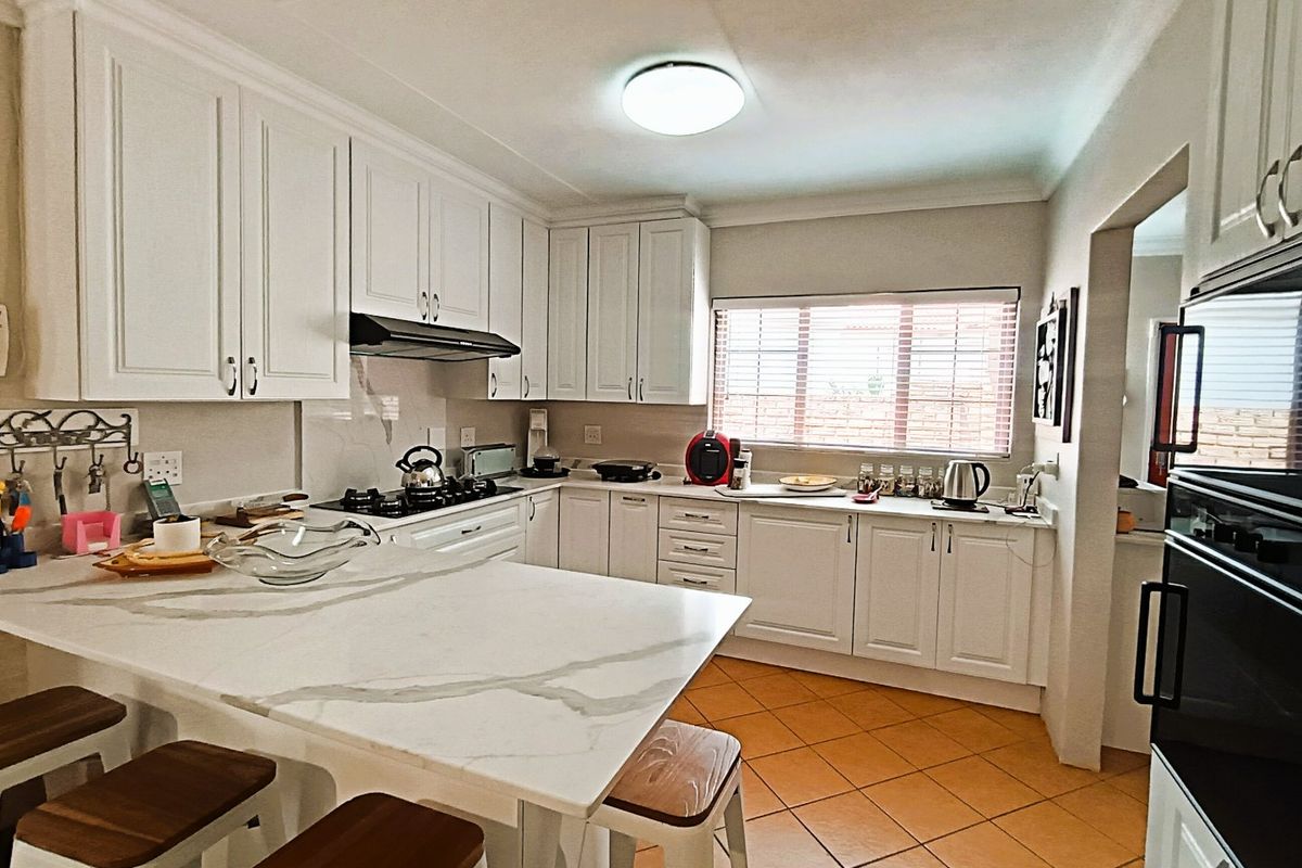 A well-maintained kitchen featuring white cabinetry, marble-look countertops, a gas hob, built-in oven, and tiled flooring with a breakfast nook.
