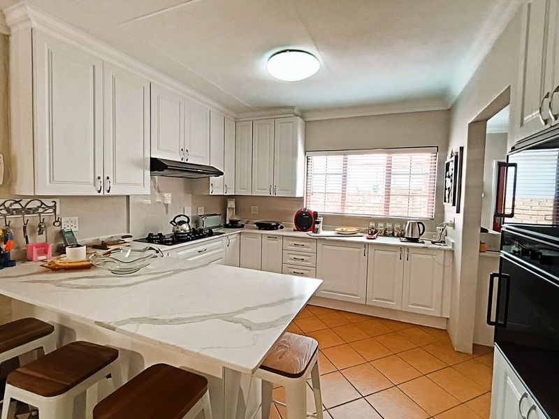 A well-maintained kitchen featuring white cabinetry, marble-look countertops, a gas hob, built-in oven, and tiled flooring with a breakfast nook.