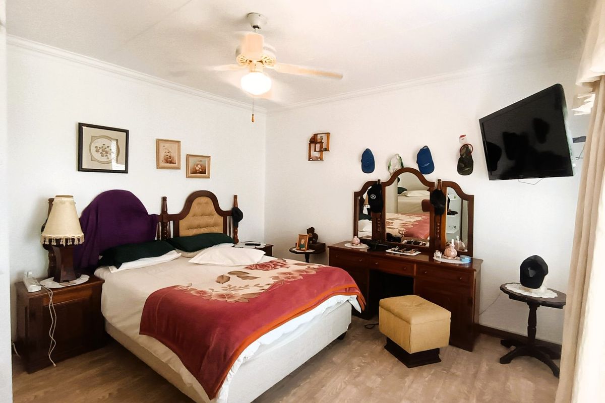 A spacious bedroom featuring light-toned laminate flooring, a central ceiling fan, and classic coving detail, offering a comfortable and functional living space.
