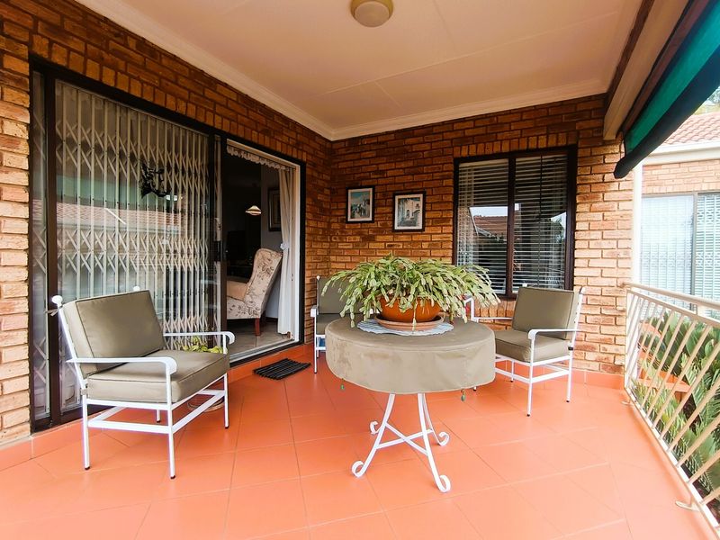 A covered patio featuring exposed brick walls, tiled flooring, and a sliding glass door with security gate, providing a comfortable outdoor living space.