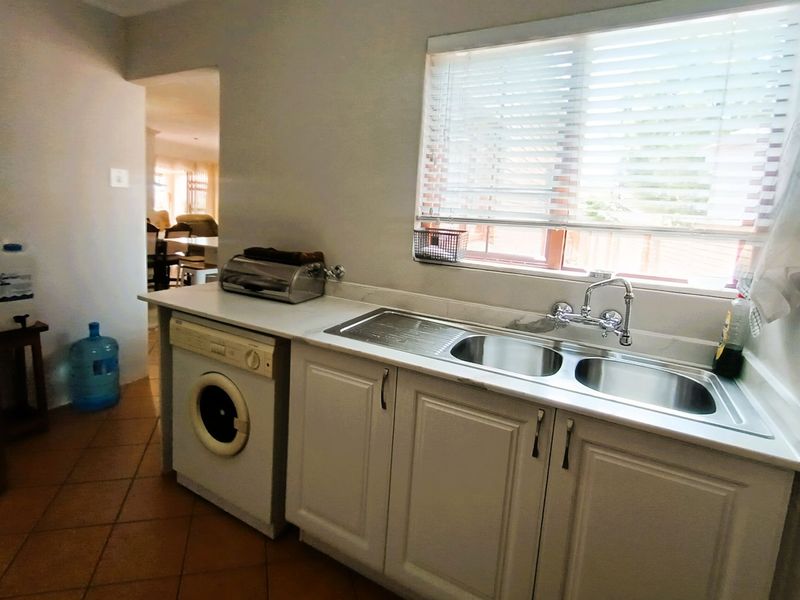 Functional laundry area featuring built-in cabinetry, a double bowl stainless steel sink with chrome mixer tap, and tiled flooring.