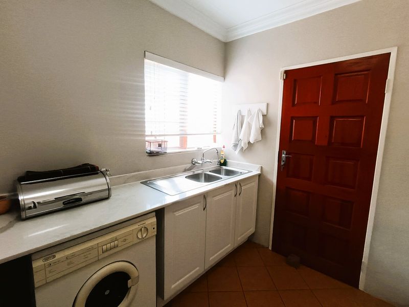 A functional laundry room featuring built-in cabinetry, a stainless steel double sink, tiled flooring, and direct access via a solid timber door.