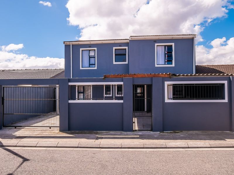 Front elevation of a two-story house featuring a secure perimeter wall, sliding driveway gate, pedestrian entrance, and modern blue exterior finish.