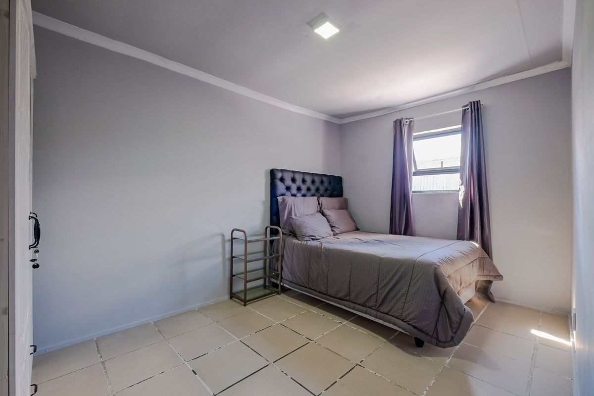 A simple bedroom featuring tiled flooring, neutral wall paint, and a top-hung window, providing a functional and clean living space.