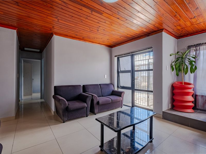 A living room featuring a warm timber tongue and groove ceiling, neutral tiled flooring, and an aluminium-framed door with integrated security gate.