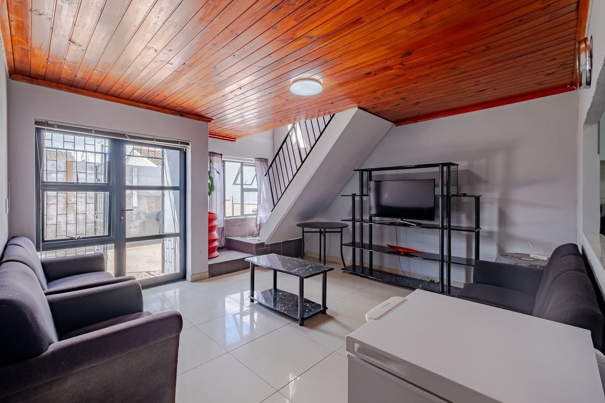 Living room featuring a warm timber ceiling, tiled flooring, and a staircase with metal railing, providing access to an outdoor area through glass doors.