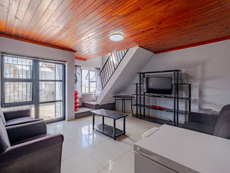 Living room featuring a warm timber ceiling, tiled flooring, and a staircase with metal railing, providing access to an outdoor area through glass doors.