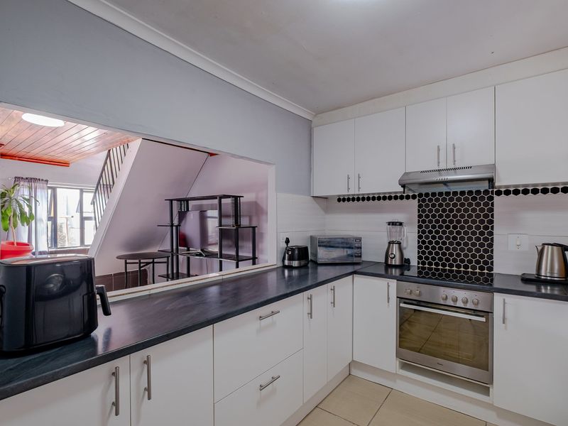 Functional kitchen featuring white cabinetry, black countertops, a built-in oven with hob, and a convenient pass-through window overlooking the adjacent living area.