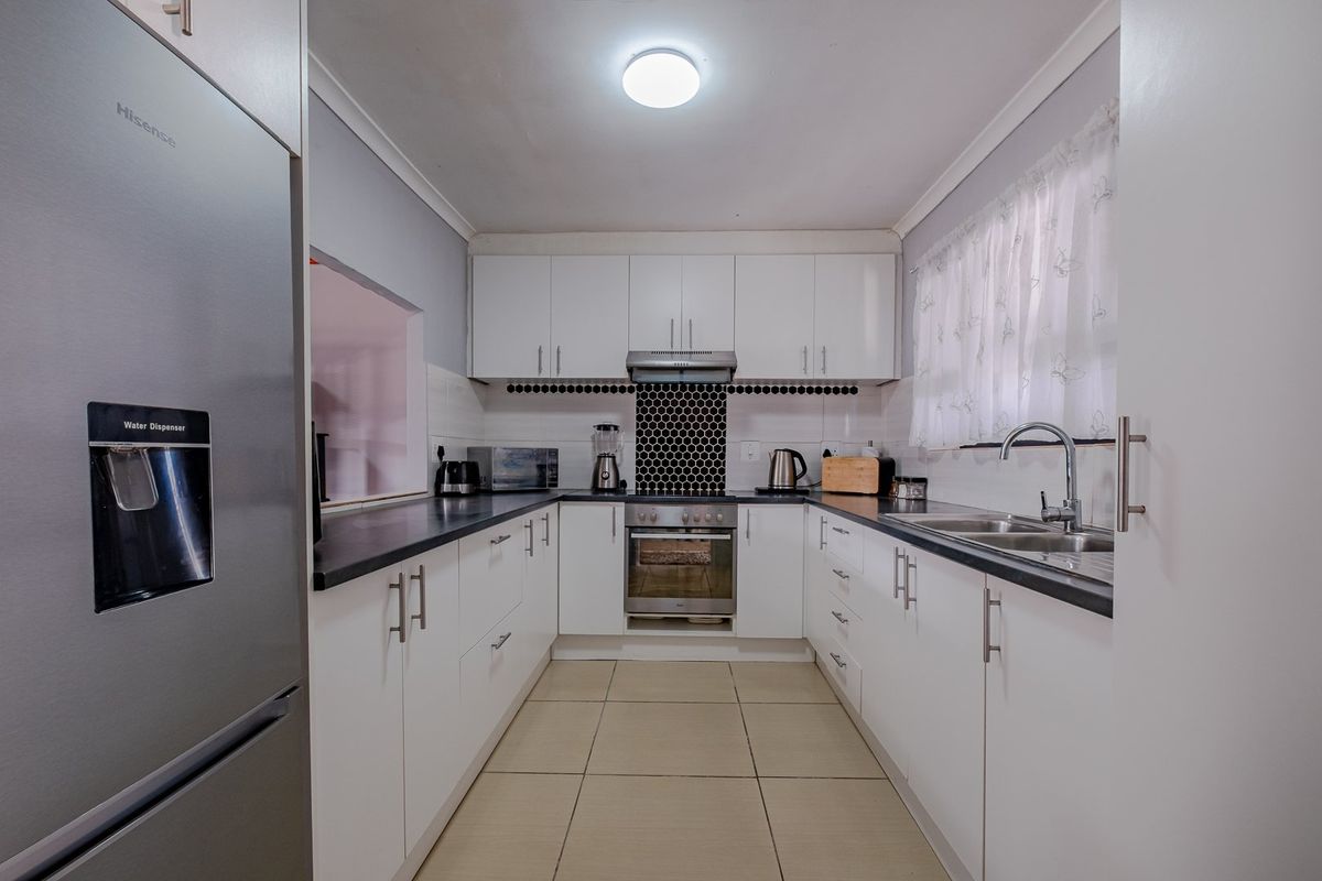 A well-maintained galley-style kitchen featuring white cabinetry, dark countertops, a stainless steel oven, and a modern tiled backsplash.