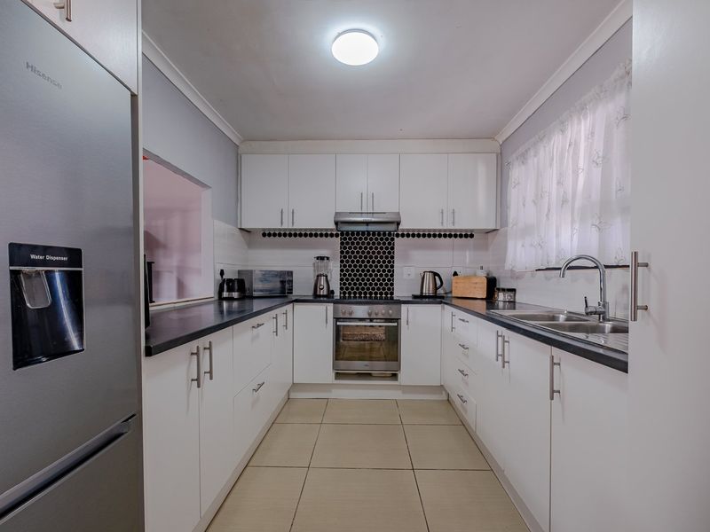 A well-maintained galley-style kitchen featuring white cabinetry, dark countertops, a stainless steel oven, and a modern tiled backsplash.