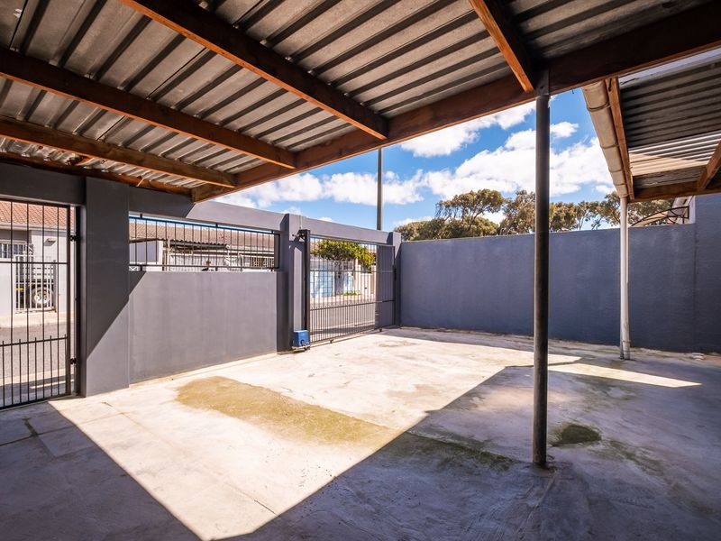 A covered outdoor parking area or garage featuring a corrugated metal roof, concrete flooring, and secure perimeter walling with a steel gate.