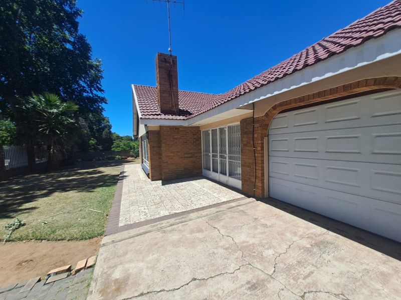 Front exterior view of a brick house featuring a tiled roof, chimney, paved driveway, and an attached garage.