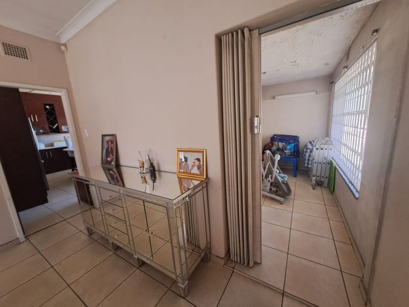 A tiled hallway area featuring a folding partition door leading to an adjacent room with security window bars.