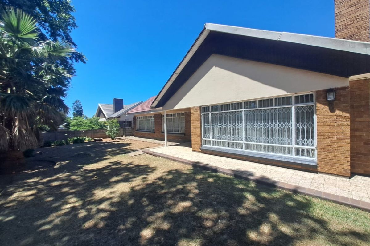Rear view of the house featuring a brick facade, tiled patio area, and large windows with security gates overlooking the garden.