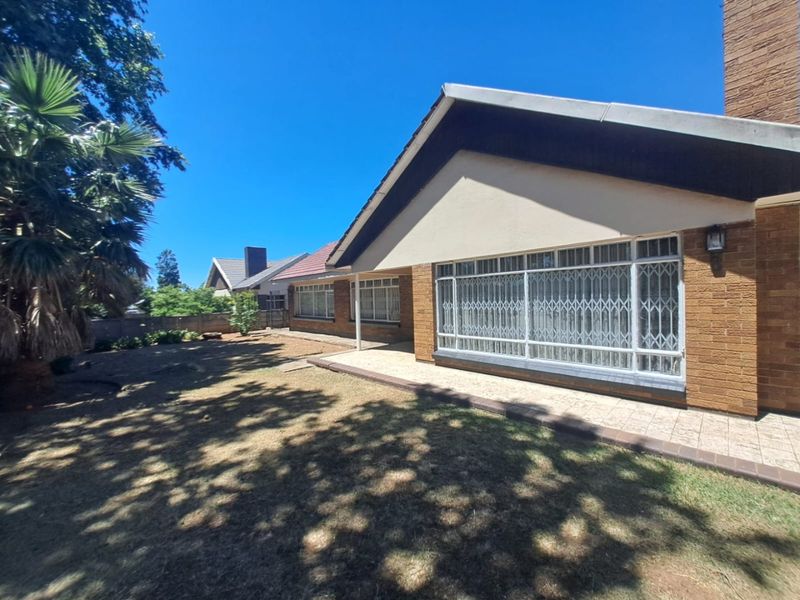 Rear view of the house featuring a brick facade, tiled patio area, and large windows with security gates overlooking the garden.