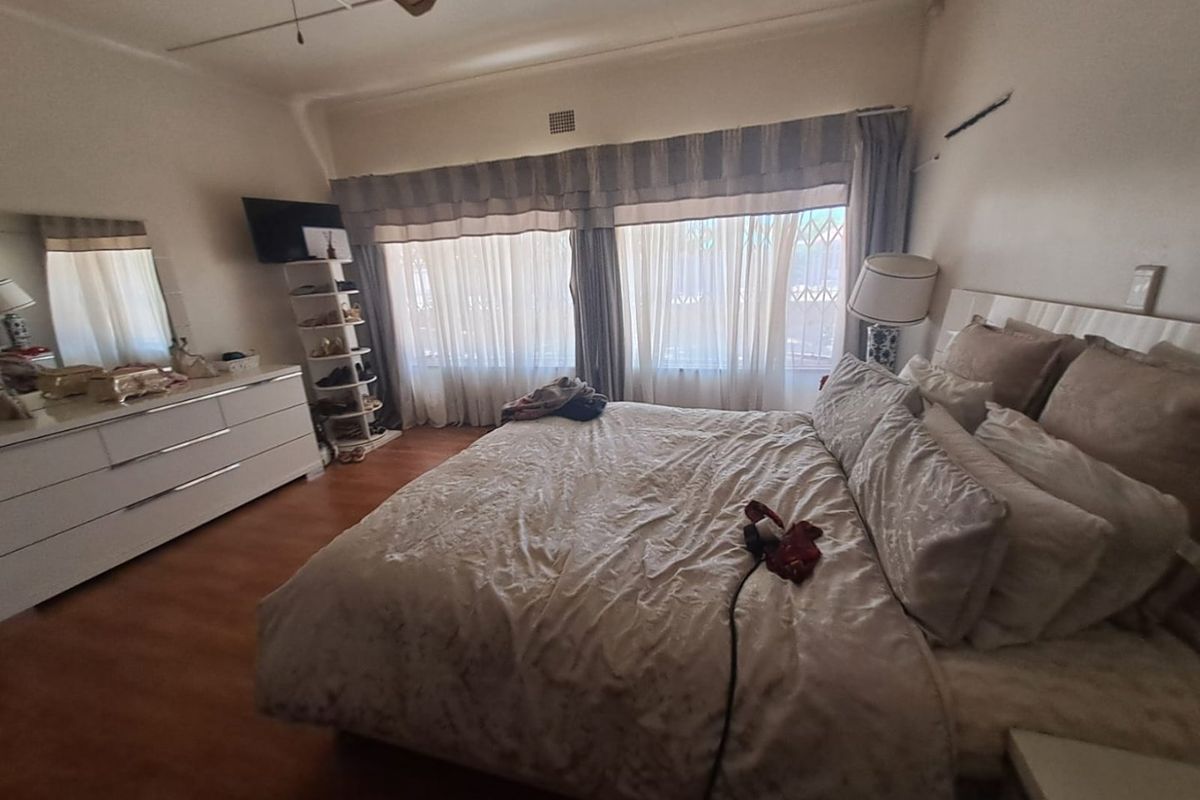 A spacious bedroom featuring laminate flooring, a ceiling fan, and large windows fitted with security bars, offering a comfortable and functional living space.