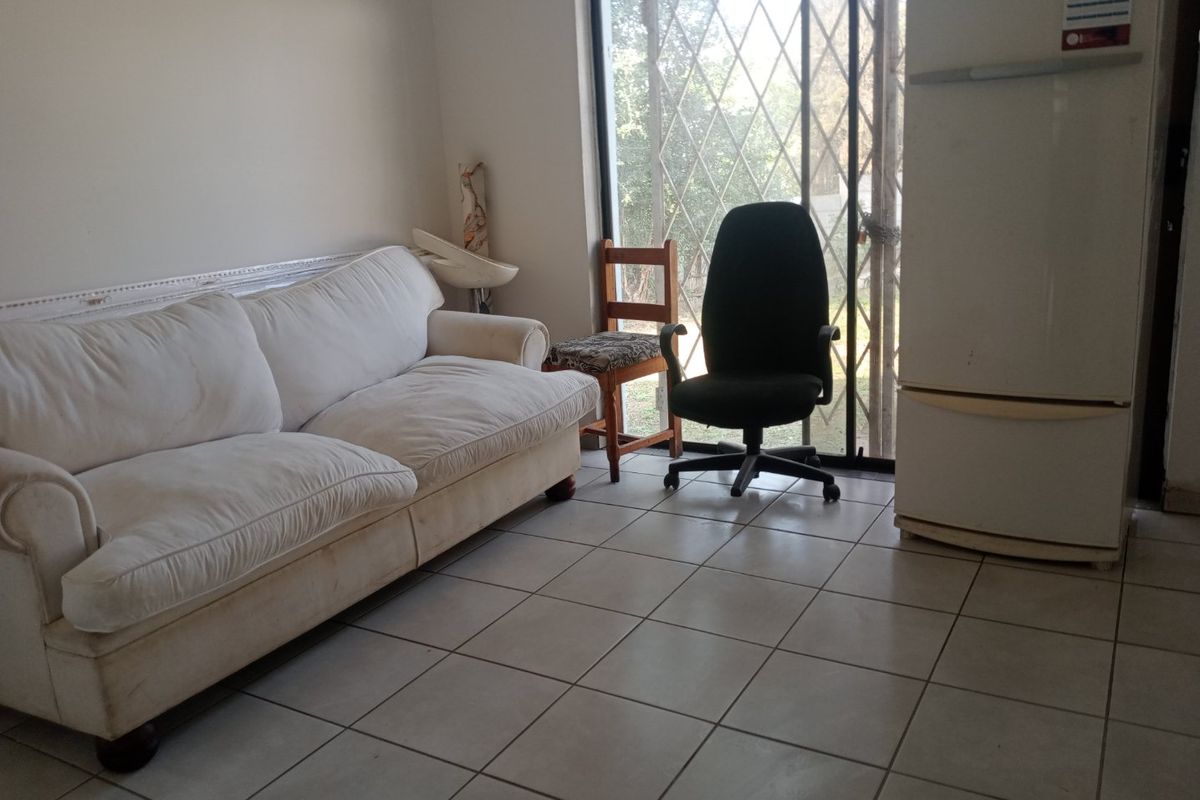 A living area featuring tiled flooring and a sliding glass door with a security gate, providing access to the exterior.