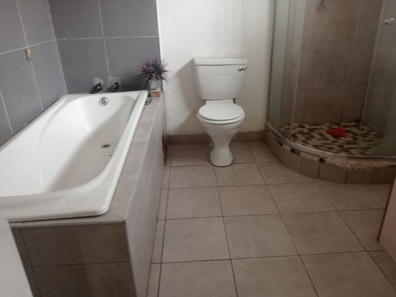 A functional bathroom featuring a built-in bathtub, a separate shower enclosure, and a toilet, finished with neutral floor and wall tiling.