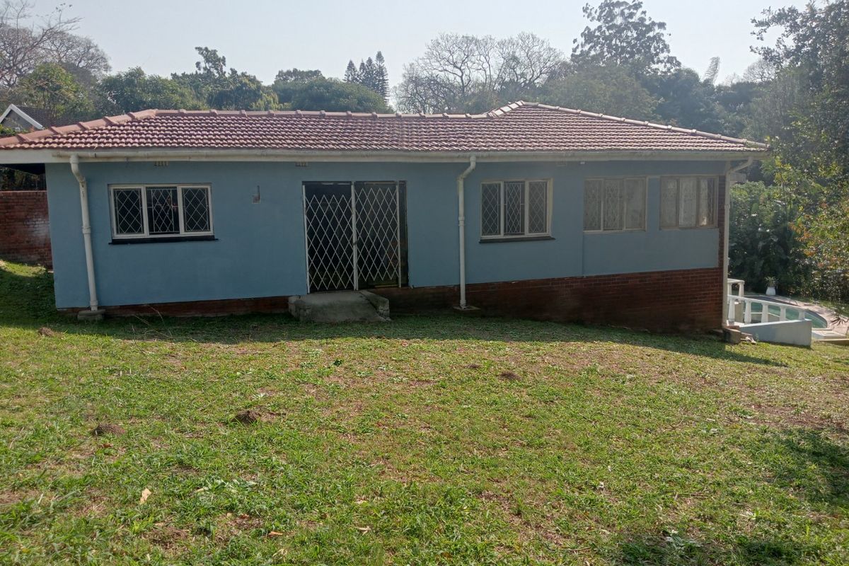 Rear view of a single-story house featuring a tiled roof, security gates, and a large garden area.