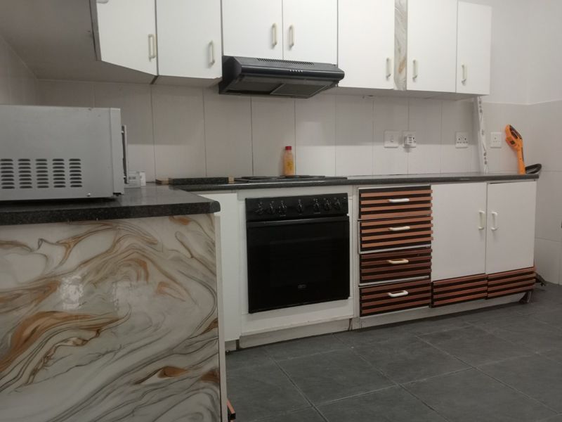 A functional kitchen featuring built-in cabinetry, a black oven and hob, extractor fan, and tiled finishes throughout.