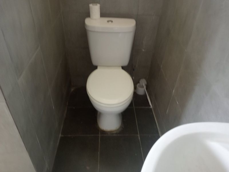 A compact bathroom featuring a standard toilet with grey wall and floor tiling.