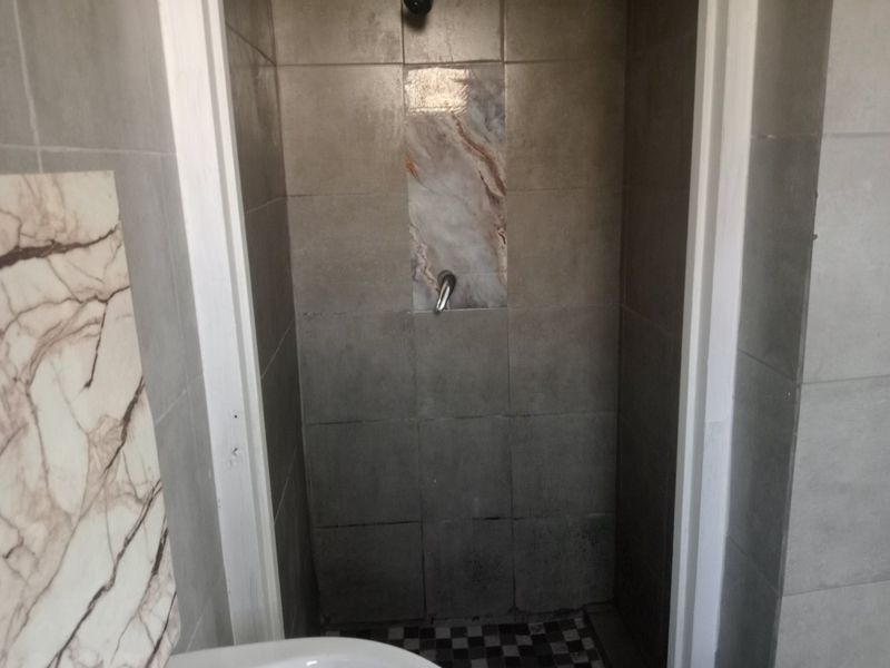 A compact shower enclosure featuring grey wall tiles, a marble-effect feature panel, and a checkered floor tile design.