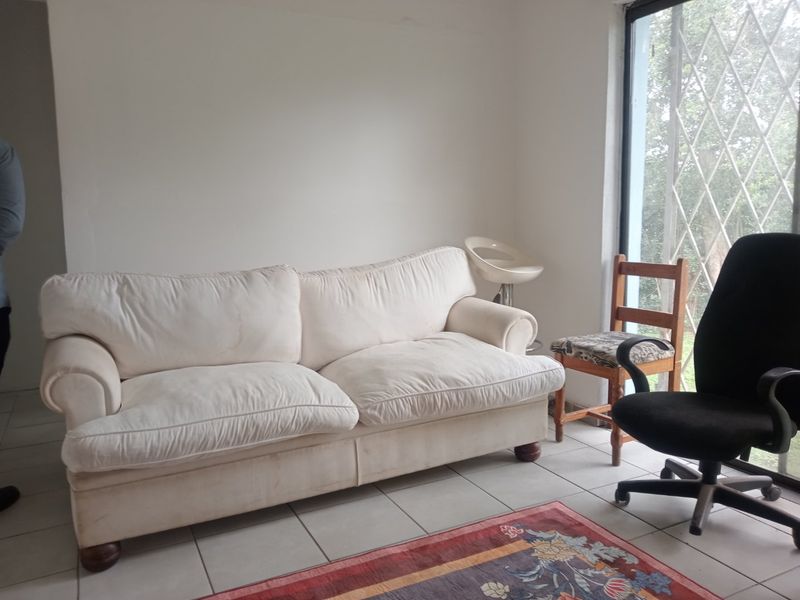 A living room area featuring neutral tiled flooring and a large window with a fitted security gate.
