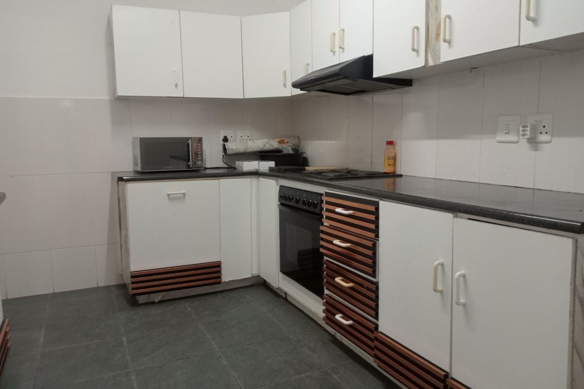 A functional kitchen featuring white cabinetry with wood-slat detailing, dark countertops, built-in oven, hob, and extractor fan with tiled splashbacks and flooring.