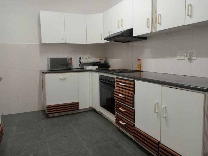 A functional kitchen featuring white cabinetry with wood-slat detailing, dark countertops, built-in oven, hob, and extractor fan with tiled splashbacks and flooring.