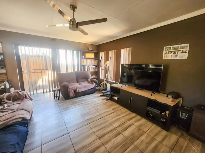 A living room featuring tiled flooring, a ceiling fan, and built-in shelving, with access to the outdoors through a sliding glass door.