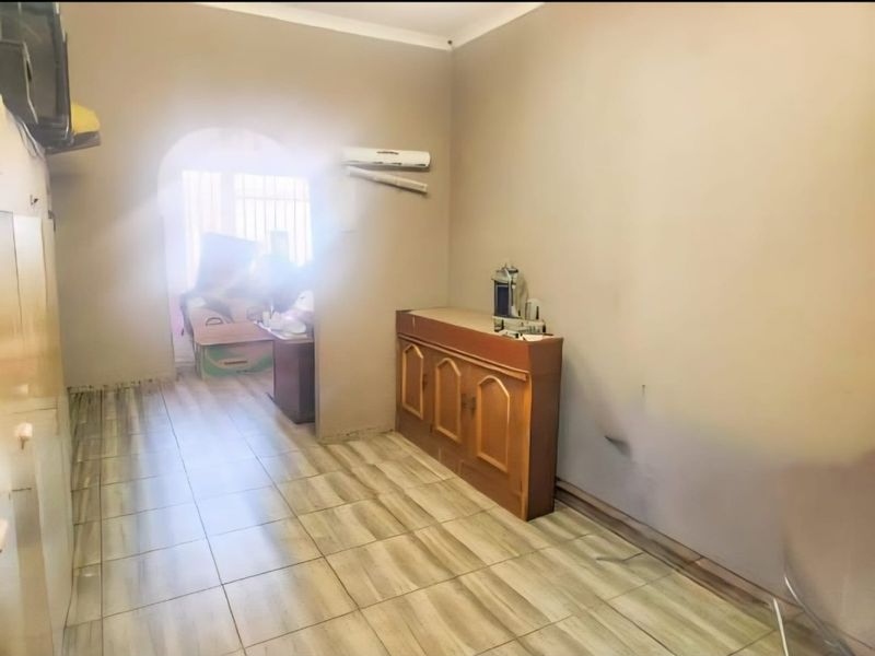 An empty living area featuring tiled flooring, an arched entryway, and a wall-mounted air conditioning unit, requiring cosmetic updates to improve its overall appeal.