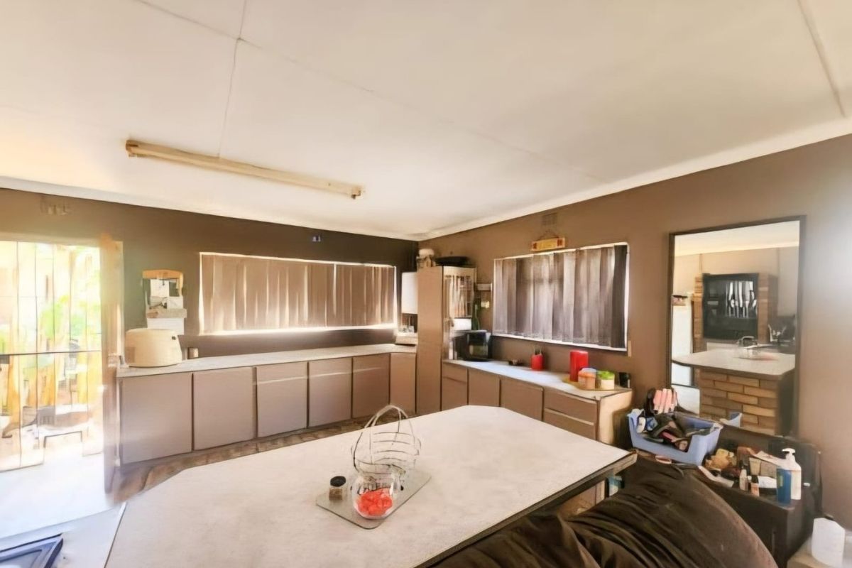 A functional kitchen space featuring extensive built-in cabinetry, laminate countertops, and natural light through vertical blinds, offering potential for modern renovation.
