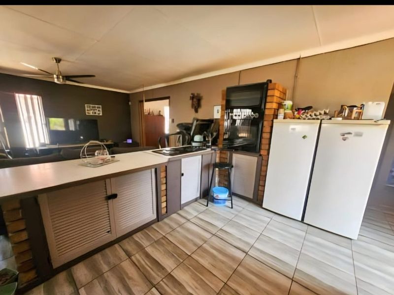 Open-plan living and kitchen area featuring tiled flooring, a central kitchen island, and a brick-encased built-in oven unit.