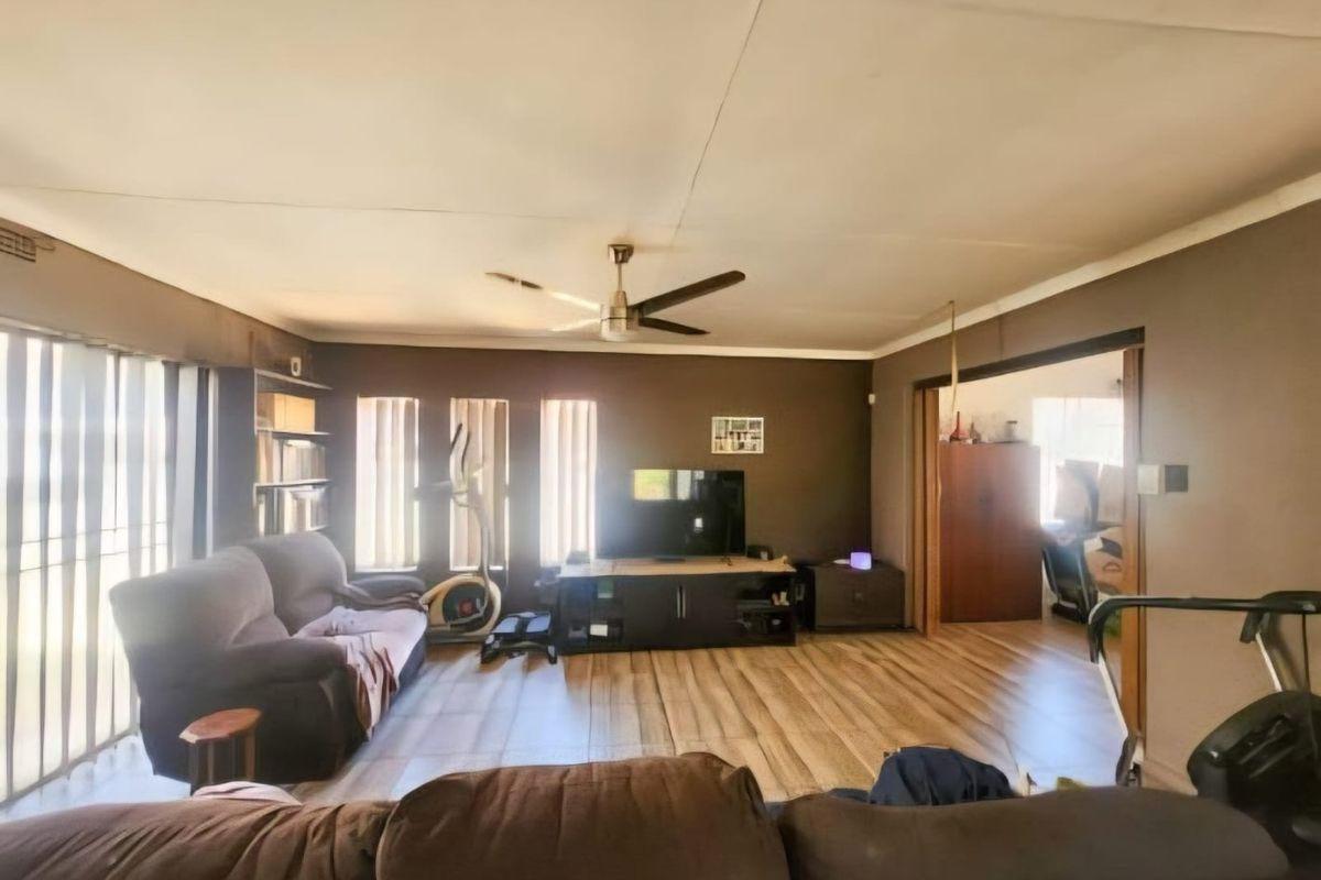 Spacious living room featuring laminate flooring, a ceiling fan, and large windows with vertical blinds, offering a comfortable and functional living space.