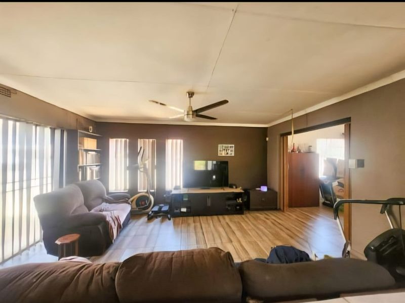 Spacious living room featuring laminate flooring, a ceiling fan, and large windows with vertical blinds, offering a comfortable and functional living space.