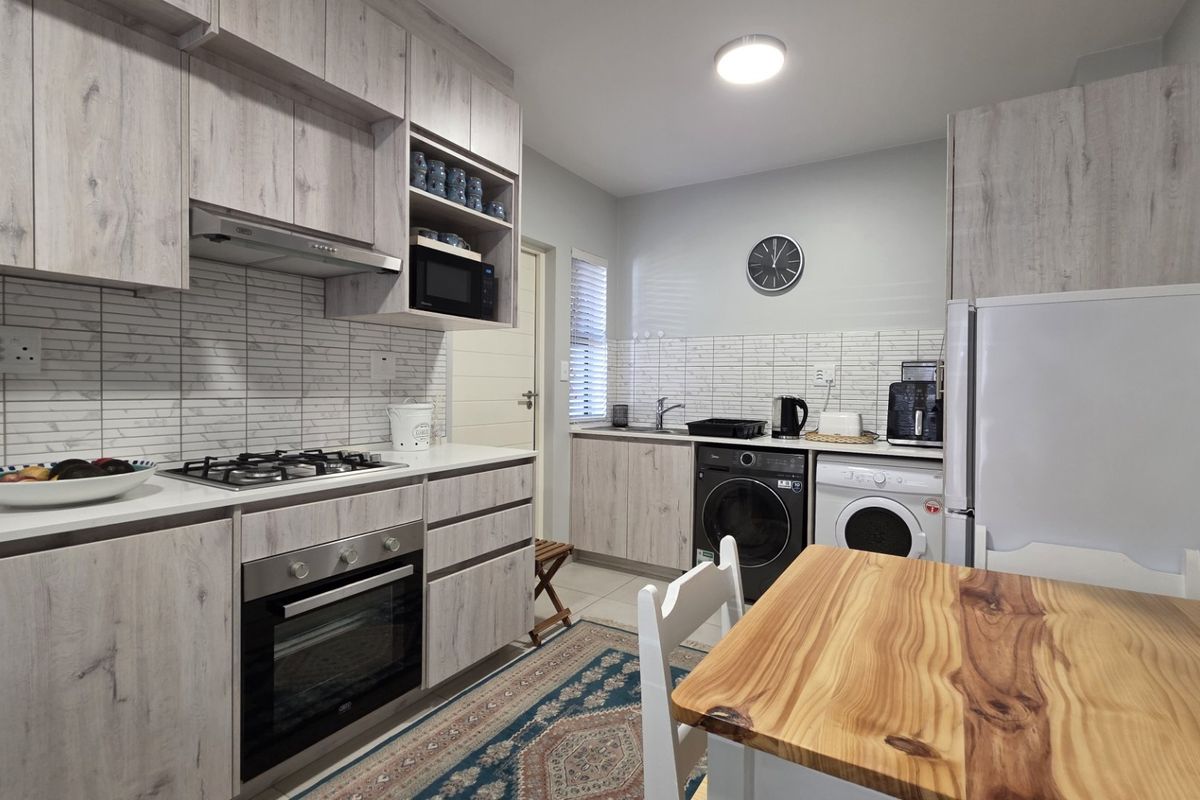 Modern kitchen featuring light wood-grain cabinetry, gas hob, built-in oven, and integrated laundry facilities with a clean tiled backsplash.